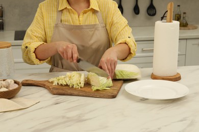 Photo of Woman cutting fresh chinese cabbage at table in kitchen, closeup