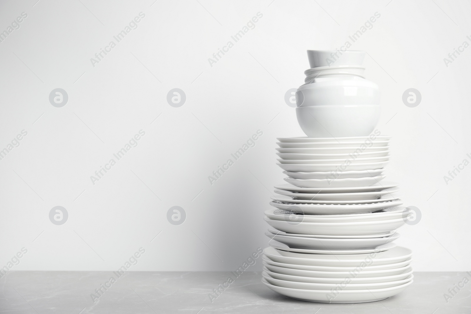 Photo of Stack of clean tableware on white table. Space for text
