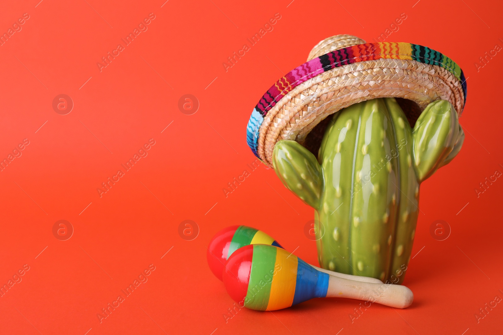 Photo of Colorful maracas and toy cactus with sombrero hat on red background, space for text. Musical instrument