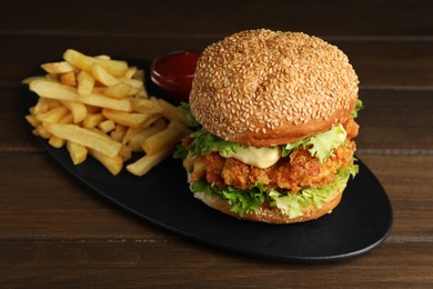 Photo of Delicious burger with crispy chicken patty, french fries and sauce on wooden table