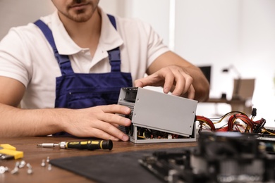 Male technician repairing power supply unit at table indoors, closeup