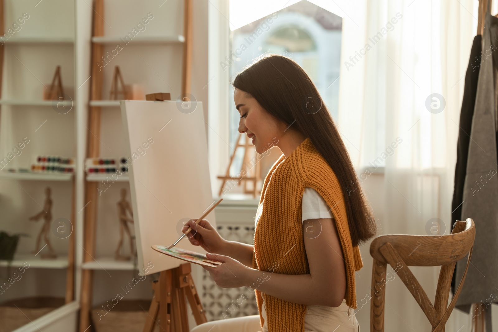 Photo of Beautiful young woman drawing on easel at home