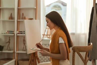 Beautiful young woman drawing on easel at home
