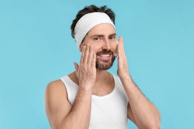 Man with headband washing his face on light blue background