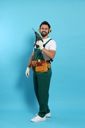 Photo of Young worker in uniform with power drill on light blue background
