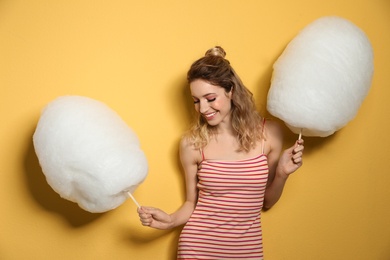 Portrait of pretty young woman with cotton candy on yellow background