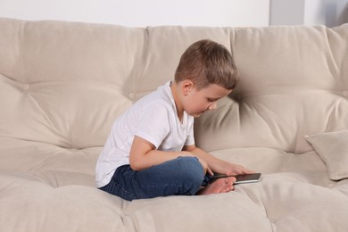 Photo of Boy with poor posture using phone on beige sofa indoors. Symptom of scoliosis