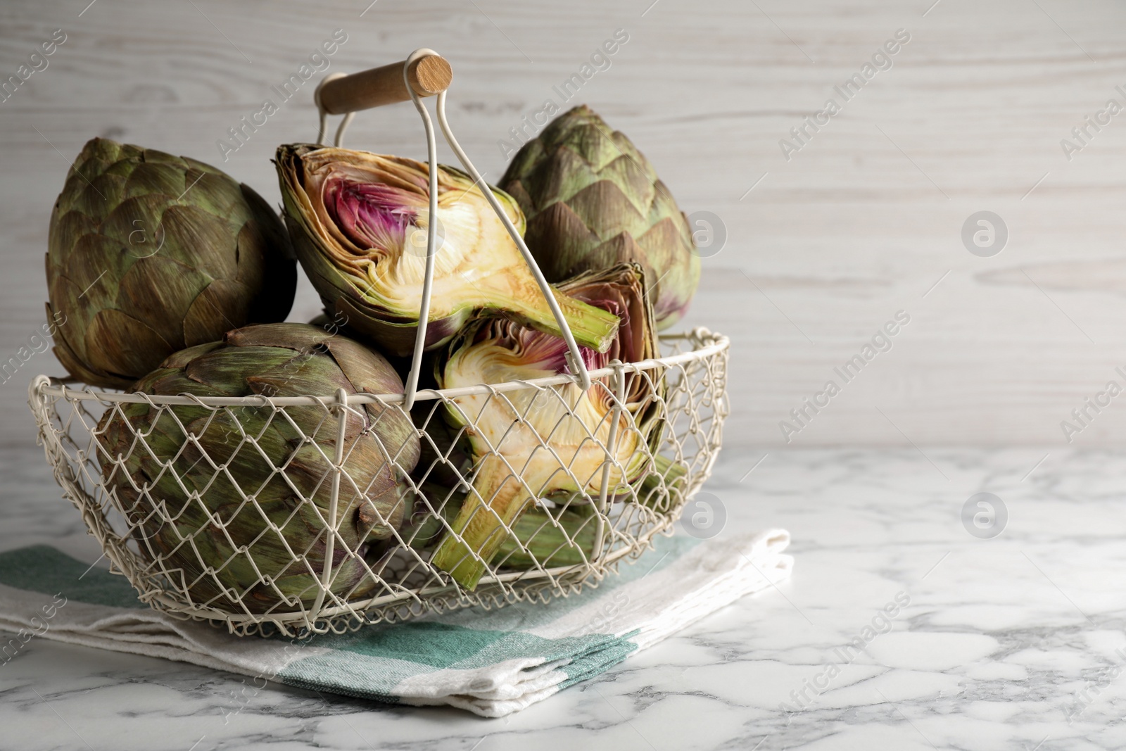 Photo of Cut and whole fresh raw artichokes on white marble table, space for text