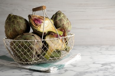 Cut and whole fresh raw artichokes on white marble table, space for text