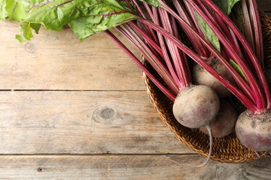 Raw ripe beets in wicker bowl on wooden table, top view. Space for text