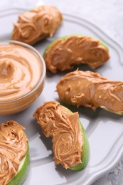 Photo of Slices of fresh green apple with peanut butter on table, closeup