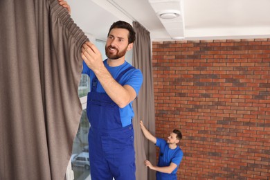 Workers in uniform hanging window curtain indoors