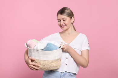 Photo of Happy woman with basket full of laundry on pink background