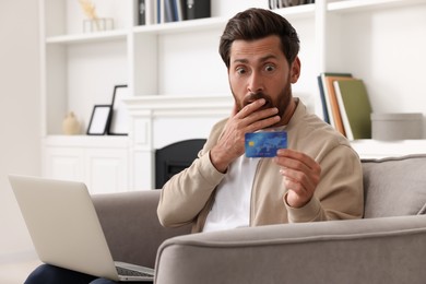 Photo of Shocked man with laptop and credit card in armchair at home. Be careful - fraud