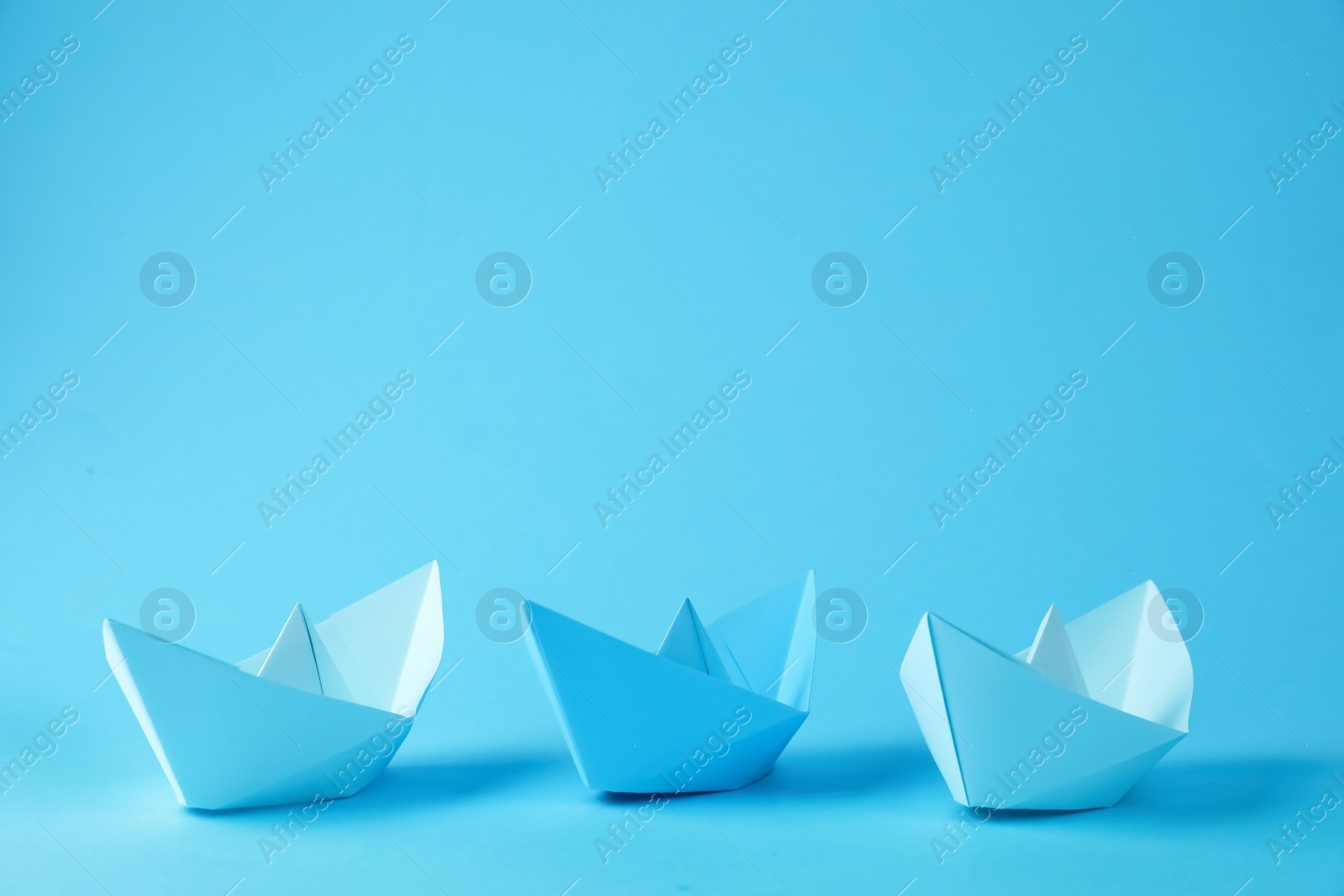 Photo of Handmade paper boats on light blue background.  Space for text