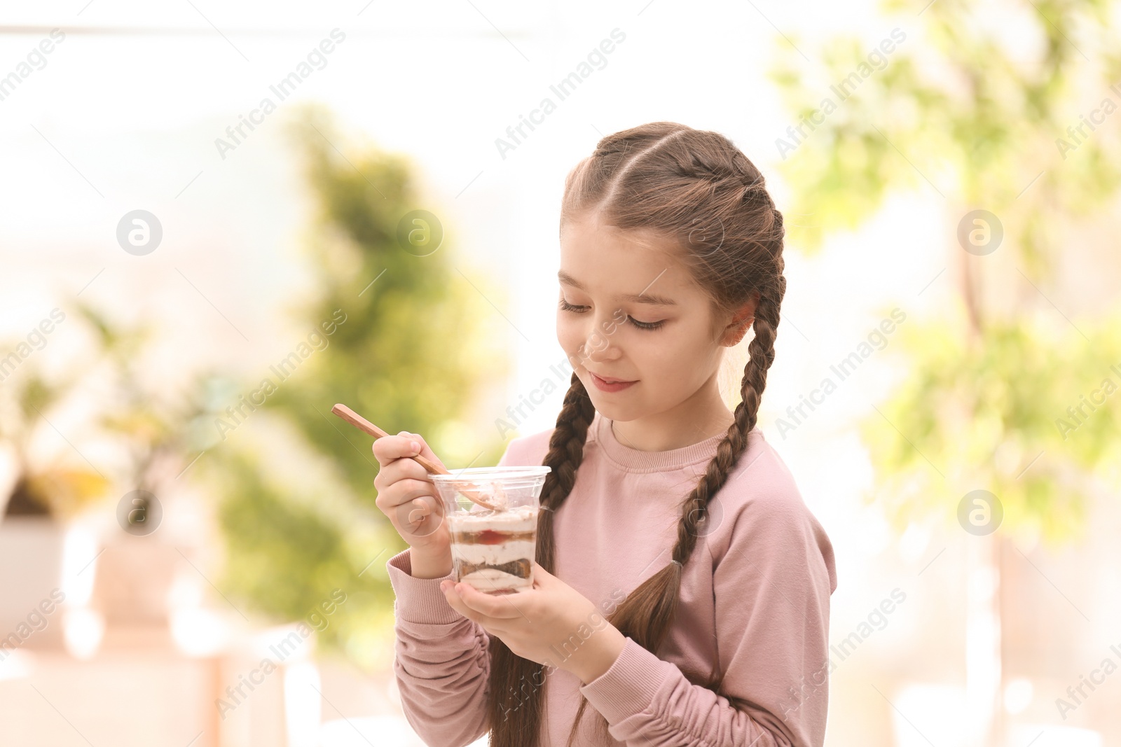 Photo of Cute girl eating tasty yogurt, indoors