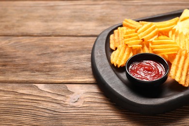 Photo of Tasty ridged chips and ketchup on wooden table, closeup. Space for text