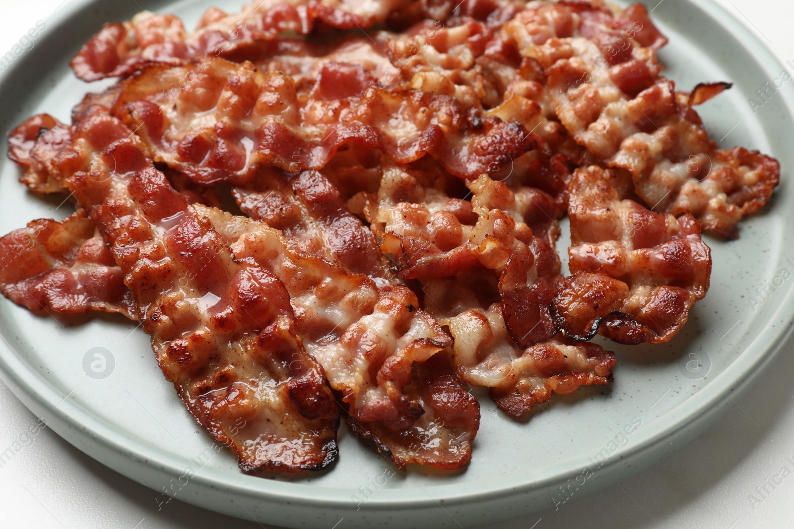 Photo of Slices of tasty fried bacon on white table, closeup