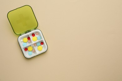 Photo of Plastic box with different pills on beige background, top view. Space for text