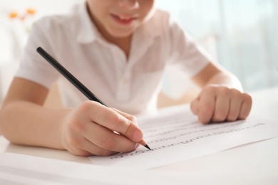 Little boy writing music notes at table, closeup