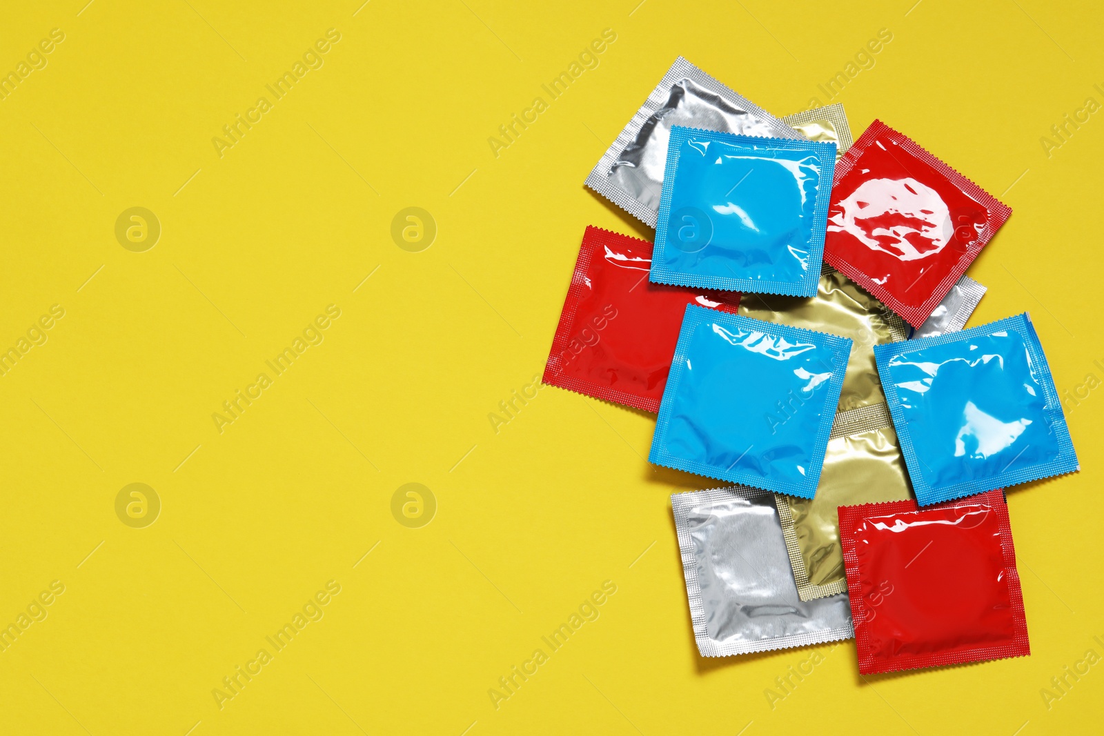 Photo of Condom packages on yellow background, flat lay and space for text. Safe sex