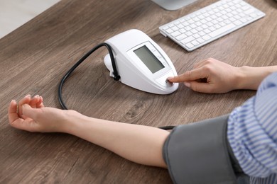 Photo of Woman measuring blood pressure at wooden table, closeup