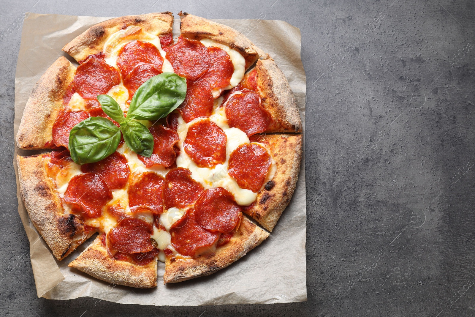 Photo of Tasty pepperoni pizza with basil on grey table, top view. Space for text