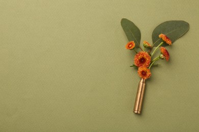 Photo of Beautiful flowers in bullet case on green background, top view. Space for text