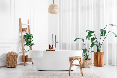 Stylish bathroom interior with beautiful tub, stool and houseplants