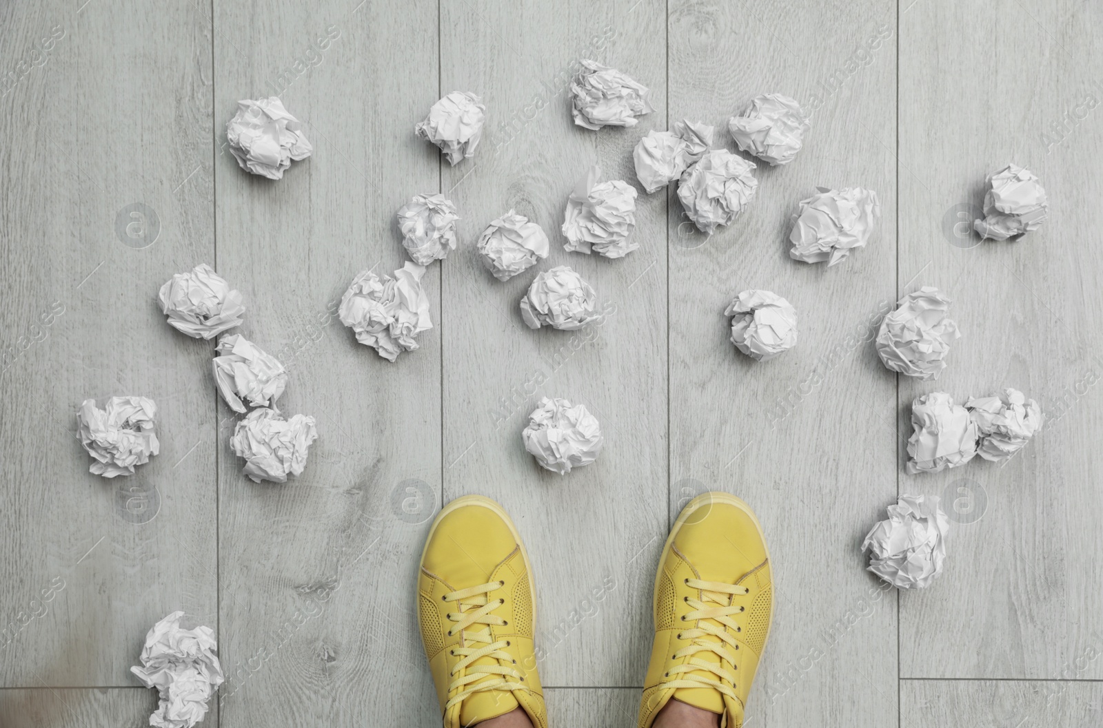 Photo of Closeup of person's feet surrounded by crumpled paper on floor, top view. Lack of ideas