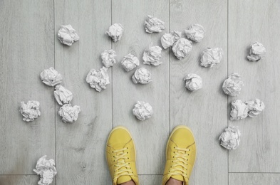 Photo of Closeup of person's feet surrounded by crumpled paper on floor, top view. Lack of ideas