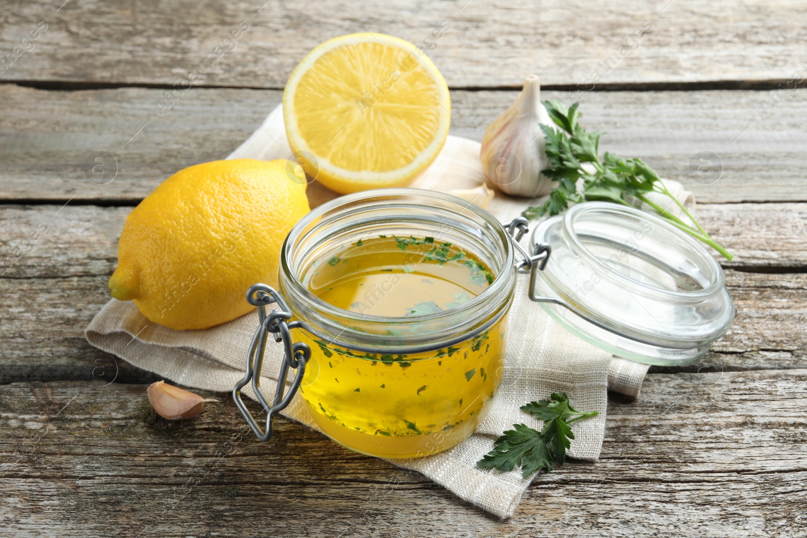 Photo of Jar with lemon sauce and ingredients on wooden table. Delicious salad dressing