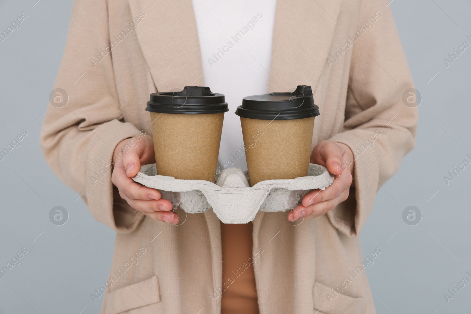 Photo of Young female intern holding takeaway cardboard cups on grey background, closeup