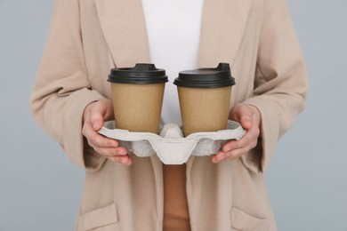 Young female intern holding takeaway cardboard cups on grey background, closeup