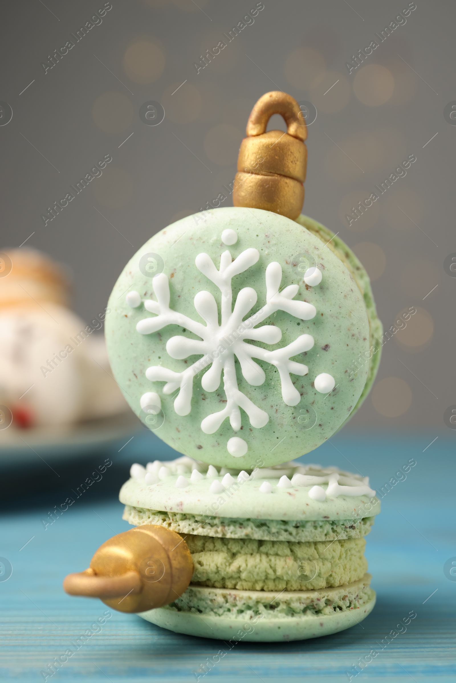 Photo of Beautifully decorated Christmas macarons on light blue wooden table against blurred festive lights, closeup