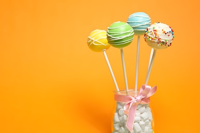 Photo of Delicious cake pops in jar full of marshmallows on color background. Space for text