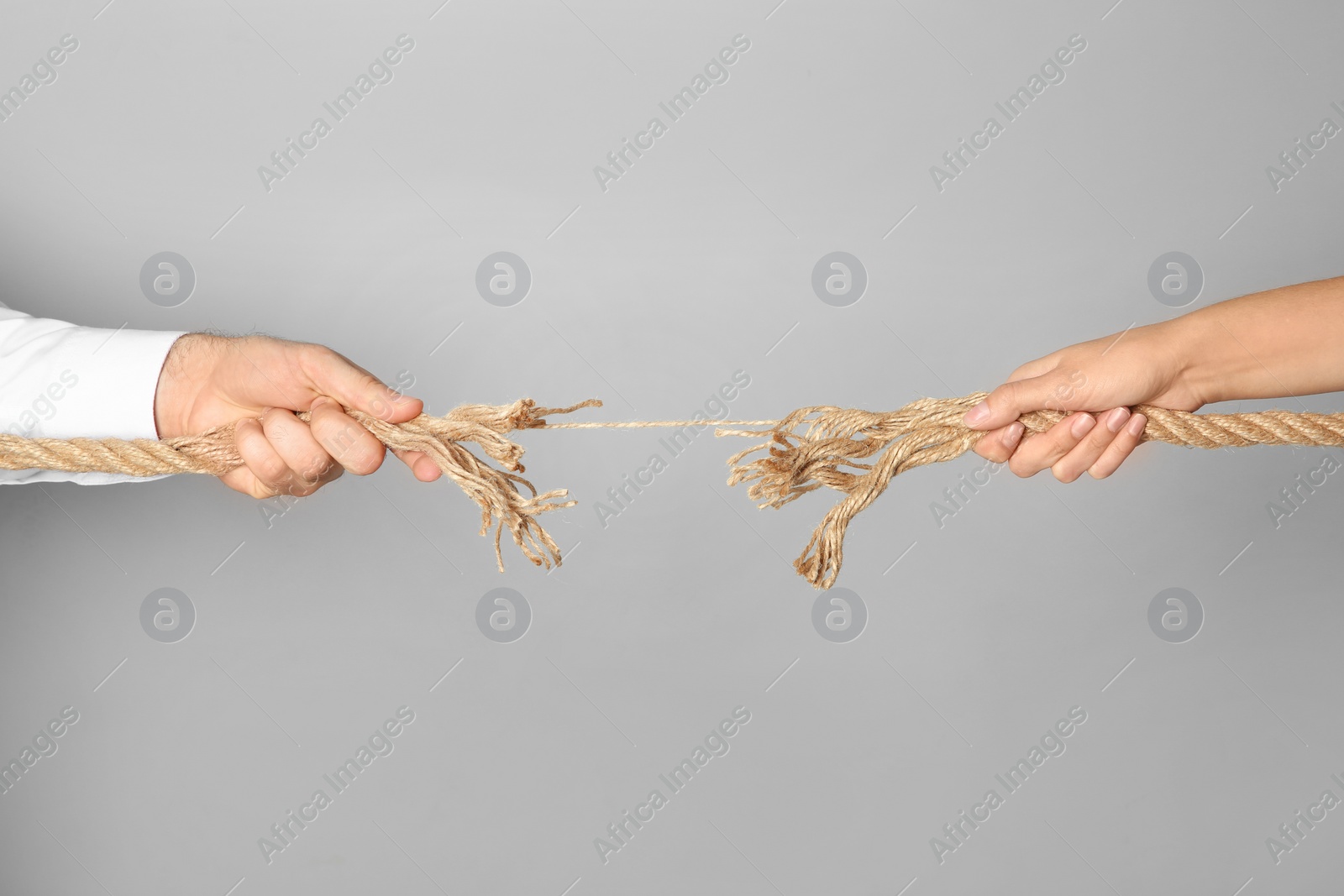 Photo of Man and woman pulling frayed rope at breaking point on gray background