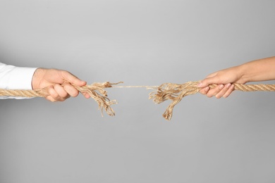 Photo of Man and woman pulling frayed rope at breaking point on gray background