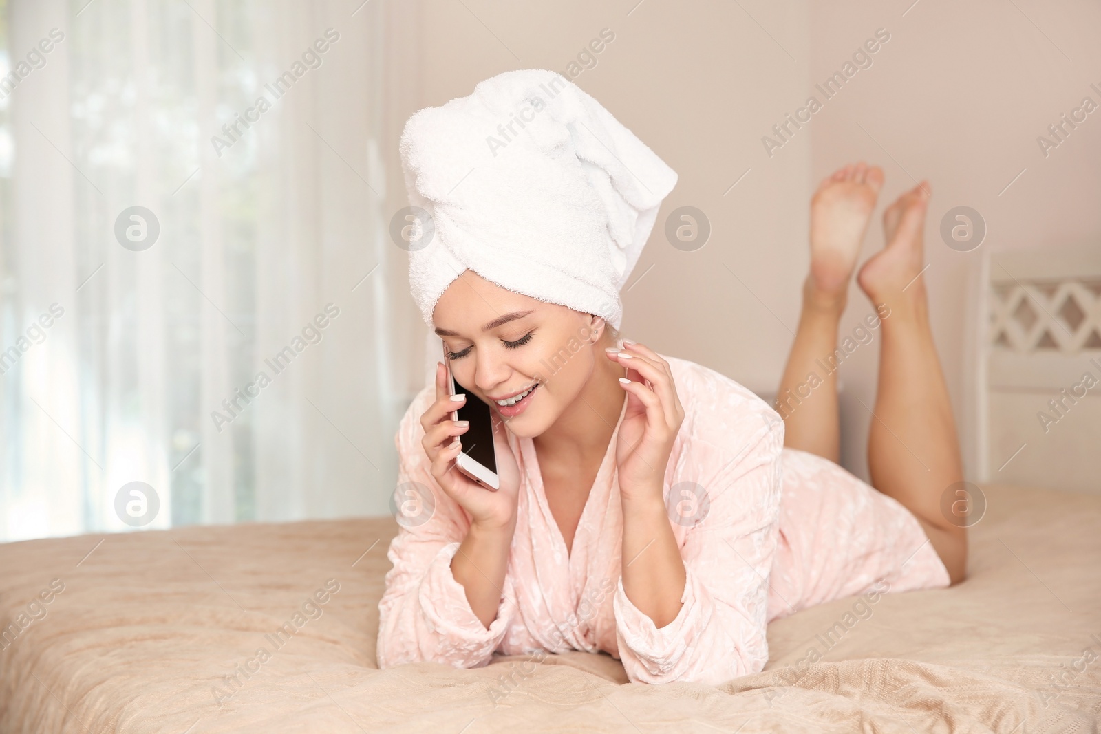 Photo of Beautiful woman with towel on head talking on phone in bedroom at home