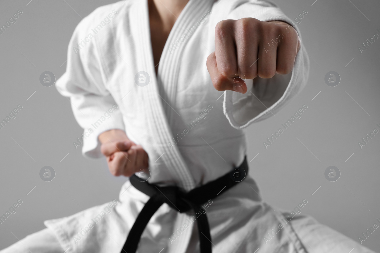 Photo of Martial arts master in keikogi with black belt against grey background, focus on fist