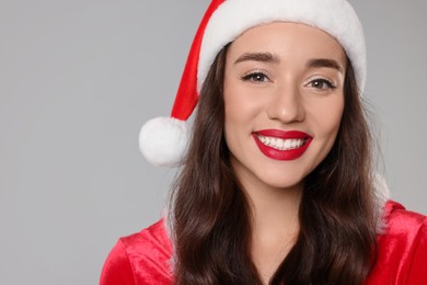Photo of Christmas celebration. Beautiful young woman in Santa hat on grey background, closeup with space for text