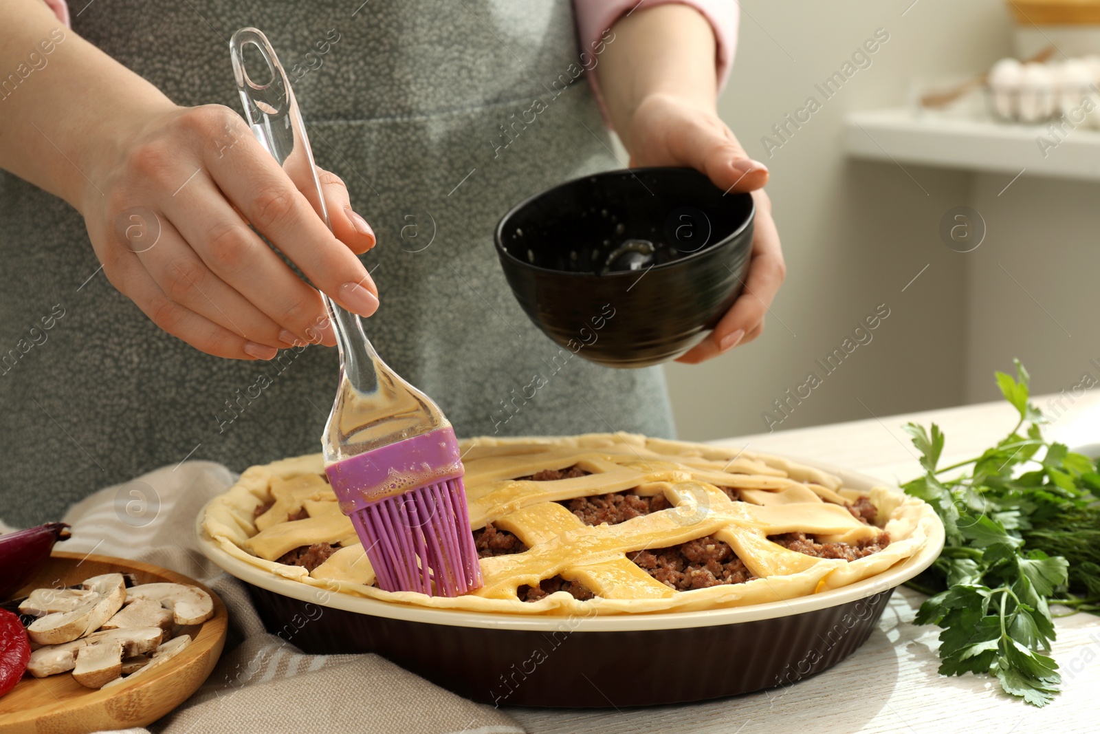Photo of Woman spreading egg yolk onto raw meat pie at white wooden table, closeup