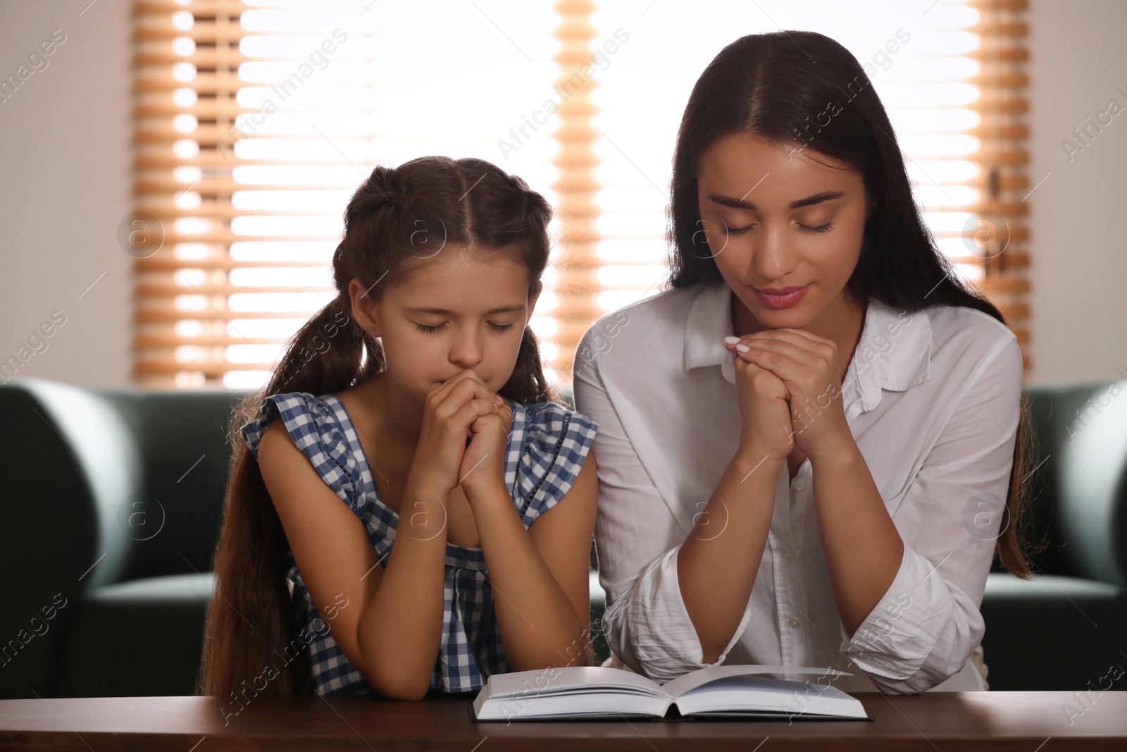 Photo of Young woman with her little daughter praying together over Bible at home