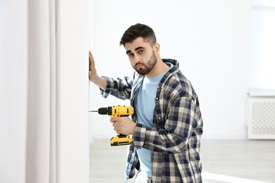 Young handyman working with electric drill at home