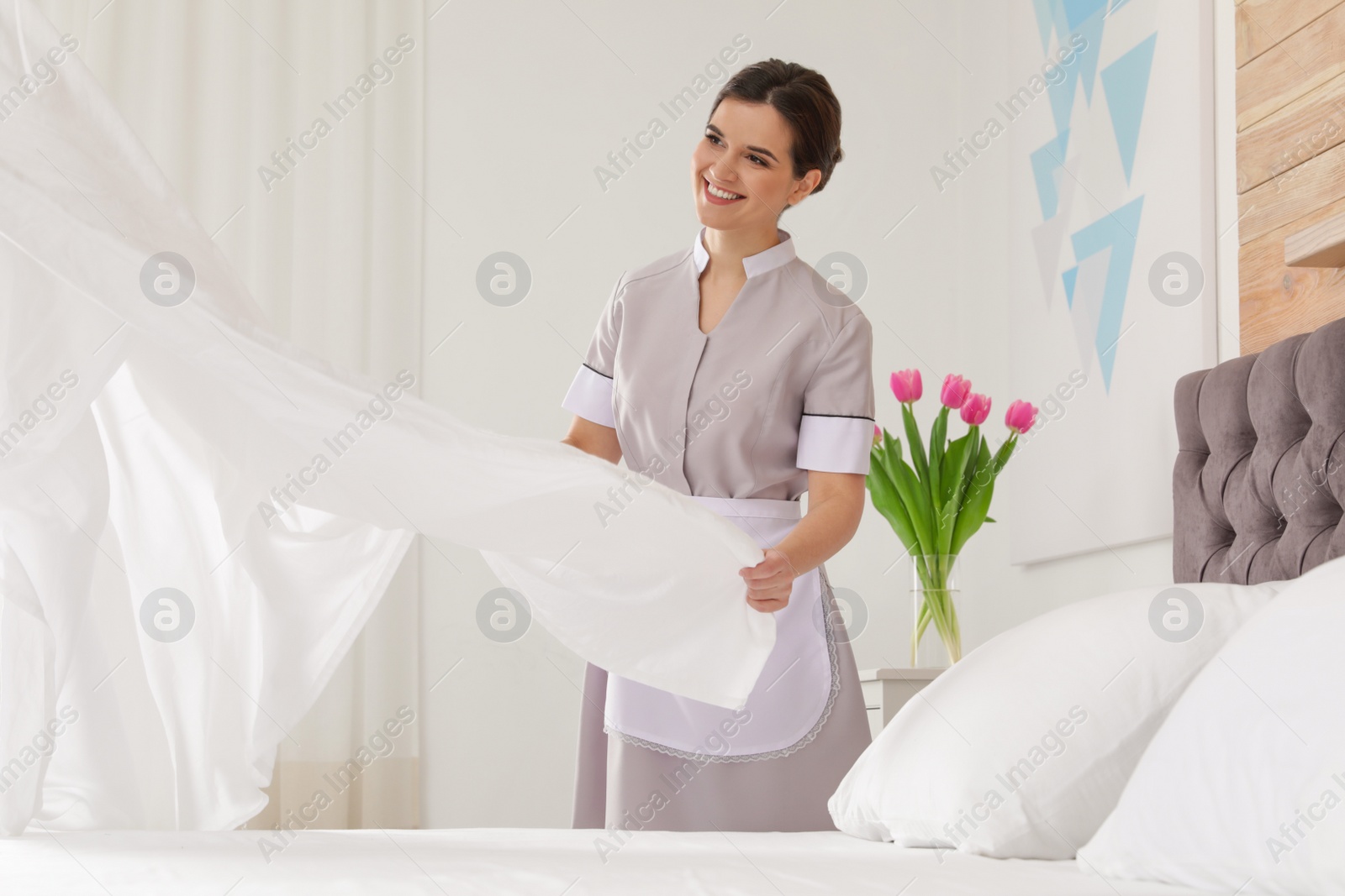 Photo of Young maid making bed in hotel room