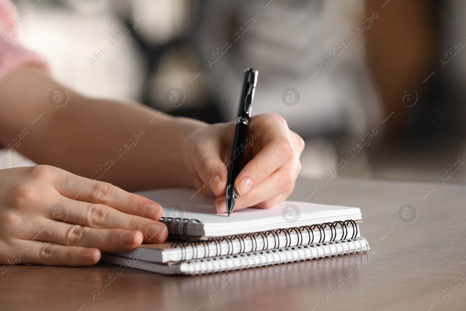 Photo of Woman writing in notebook at wooden table, closeup