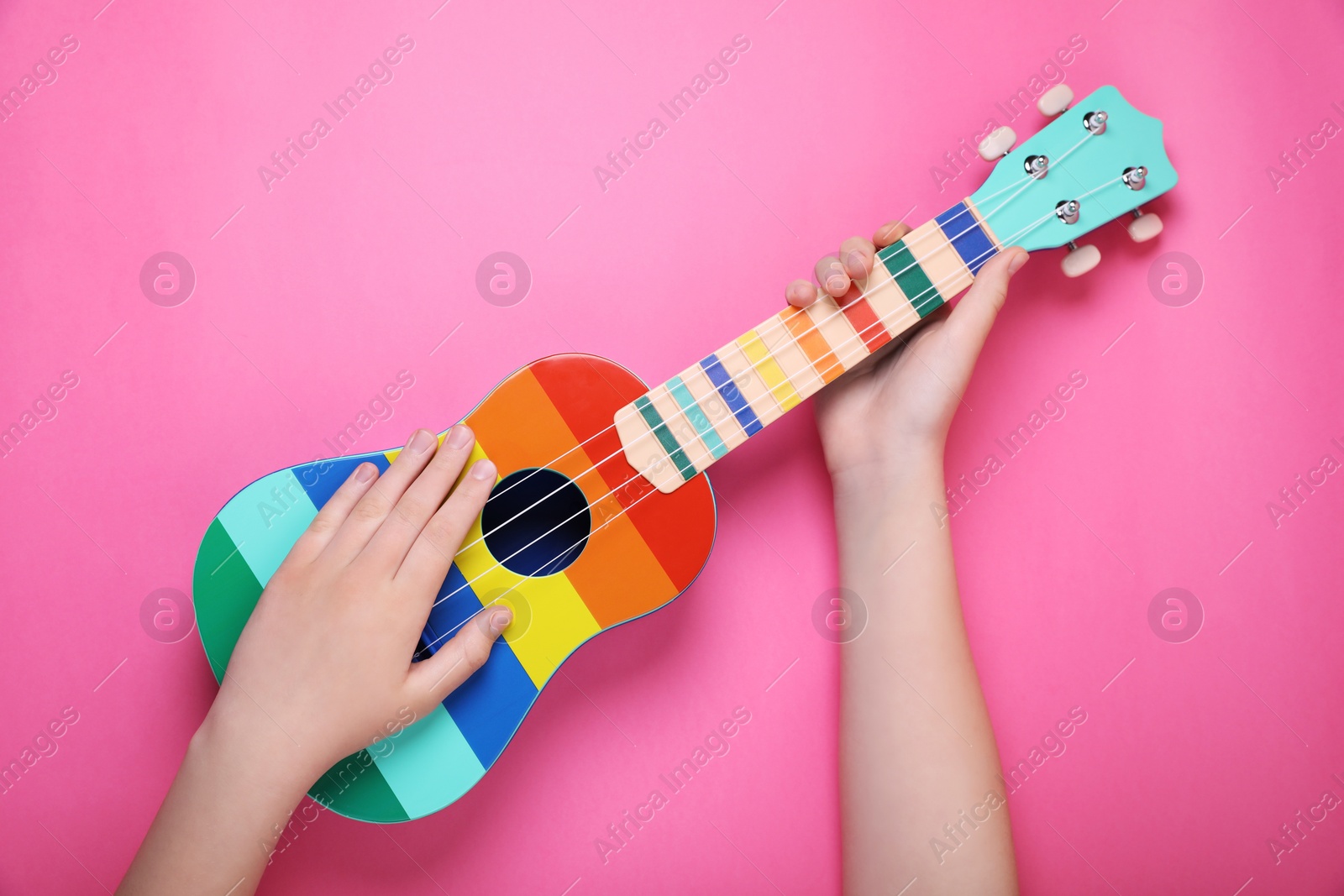 Photo of Woman holding ukulele on pink background, closeup. String musical instrument