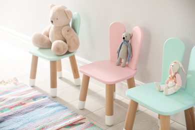 Photo of Cute toys on chairs with bunny ears near white wall indoors. Children's room interior