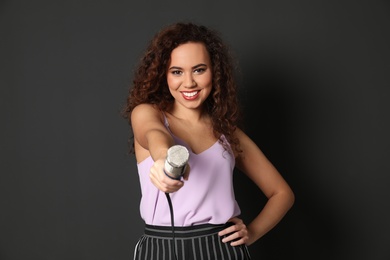 Curly African-American woman in stylish clothes holding microphone on black background