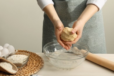 Woman kneading raw dough at white wooden table, closeup